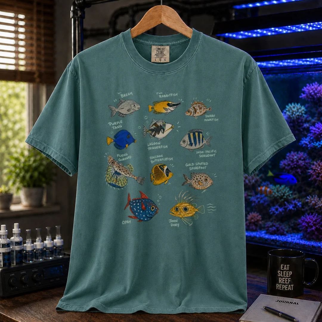 Saltwater aquarium graphic t-shirt design featuring a vintage marine species field guide layout with labeled illustrations of various fish including a Purple Tang, Lagoon Triggerfish, and Flying Gurnard, green crew neck tee