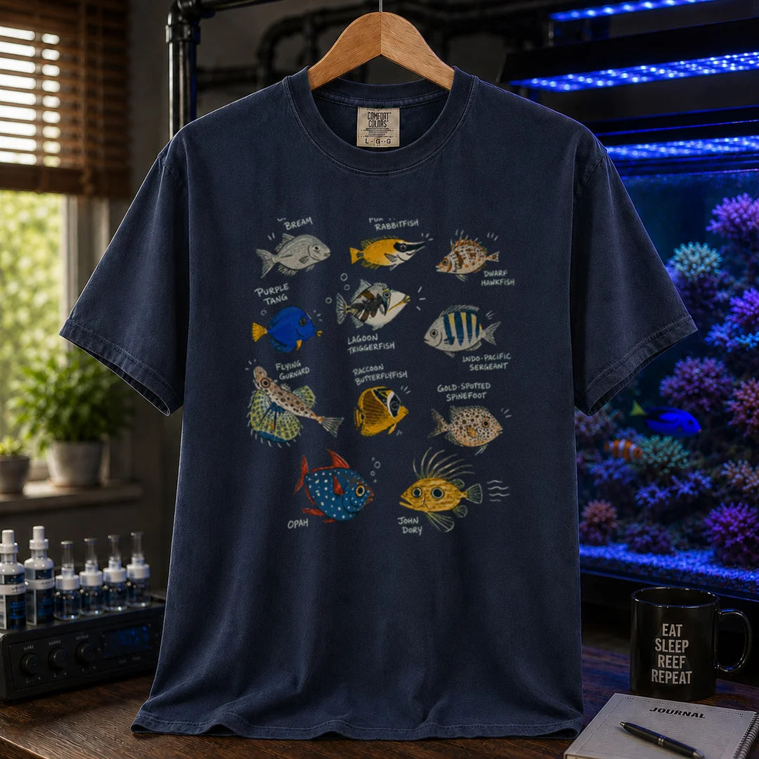 Saltwater aquarium graphic t-shirt design featuring a vintage marine species field guide layout with labeled illustrations of various fish including a Purple Tang, Lagoon Triggerfish, and Flying Gurnard, navy crew neck tee