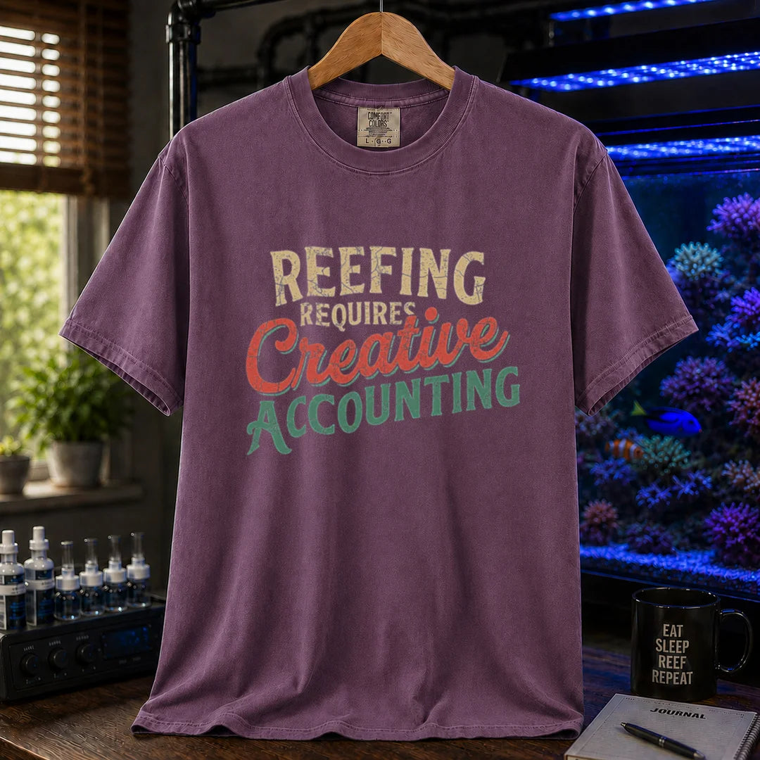 Saltwater aquarium graphic t-shirt featuring distressed retro typography in cream, red, and green reading Reefing Requires Creative Accounting, purple crew neck tee