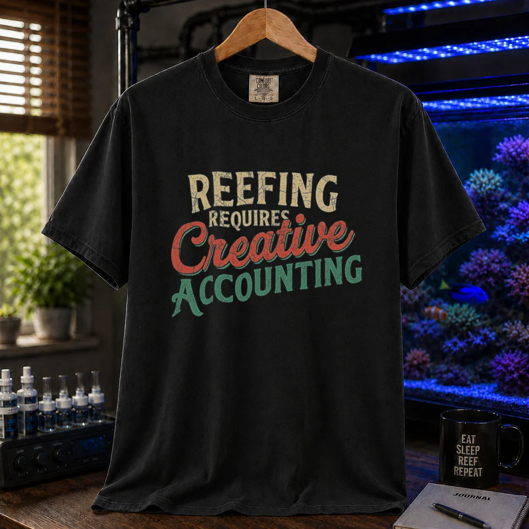Saltwater aquarium graphic t-shirt featuring distressed retro typography in cream, red, and green reading Reefing Requires Creative Accounting, black crew neck tee