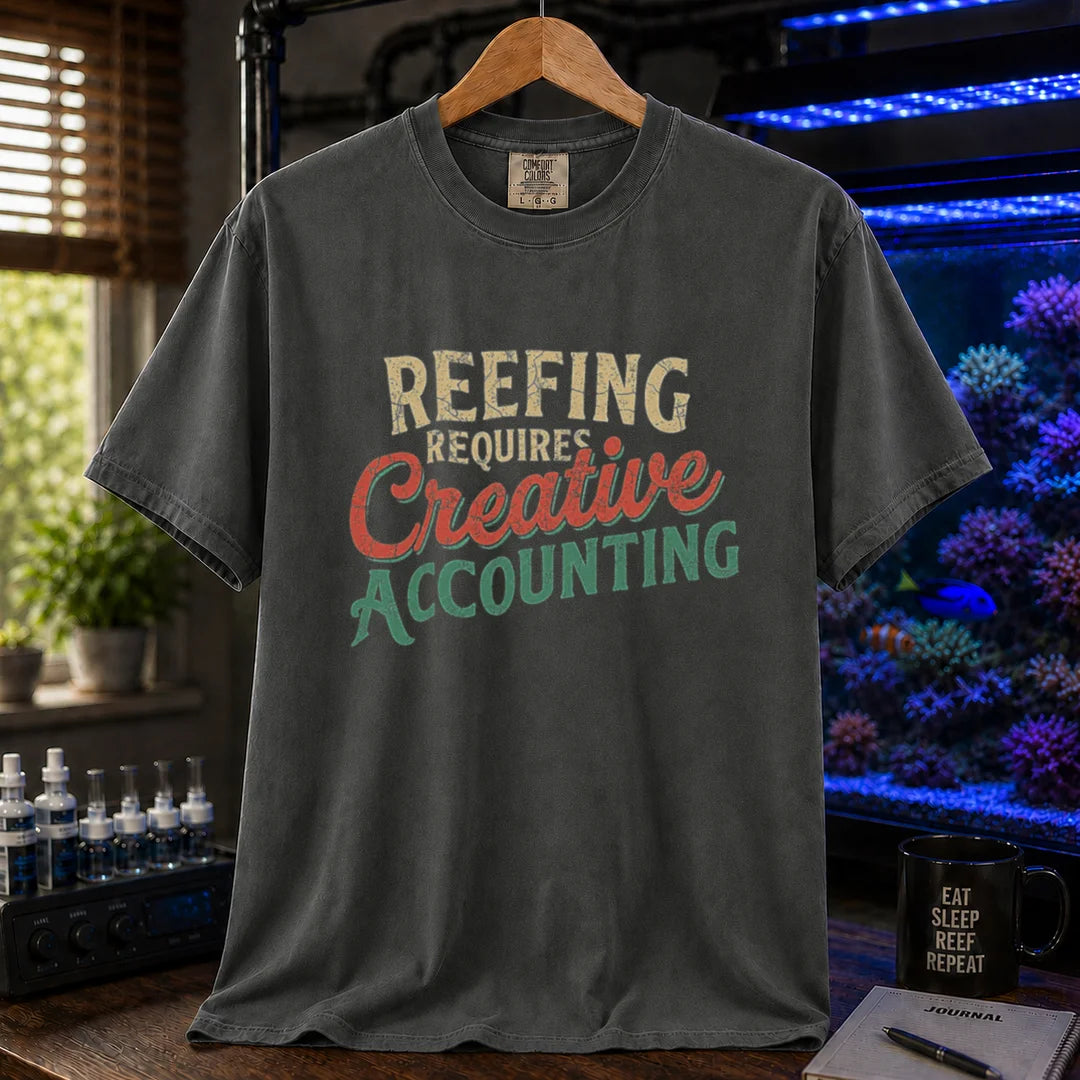 Saltwater aquarium graphic t-shirt featuring distressed retro typography in cream, red, and green reading Reefing Requires Creative Accounting, dark grey crew neck tee