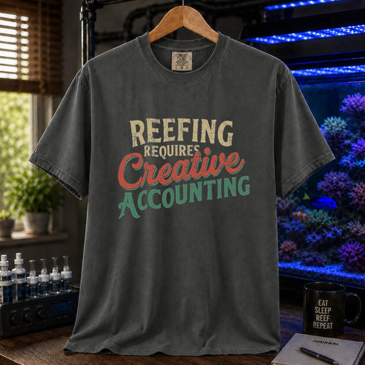 Saltwater aquarium graphic t-shirt featuring distressed retro typography in cream, red, and green reading Reefing Requires Creative Accounting, dark grey crew neck tee
