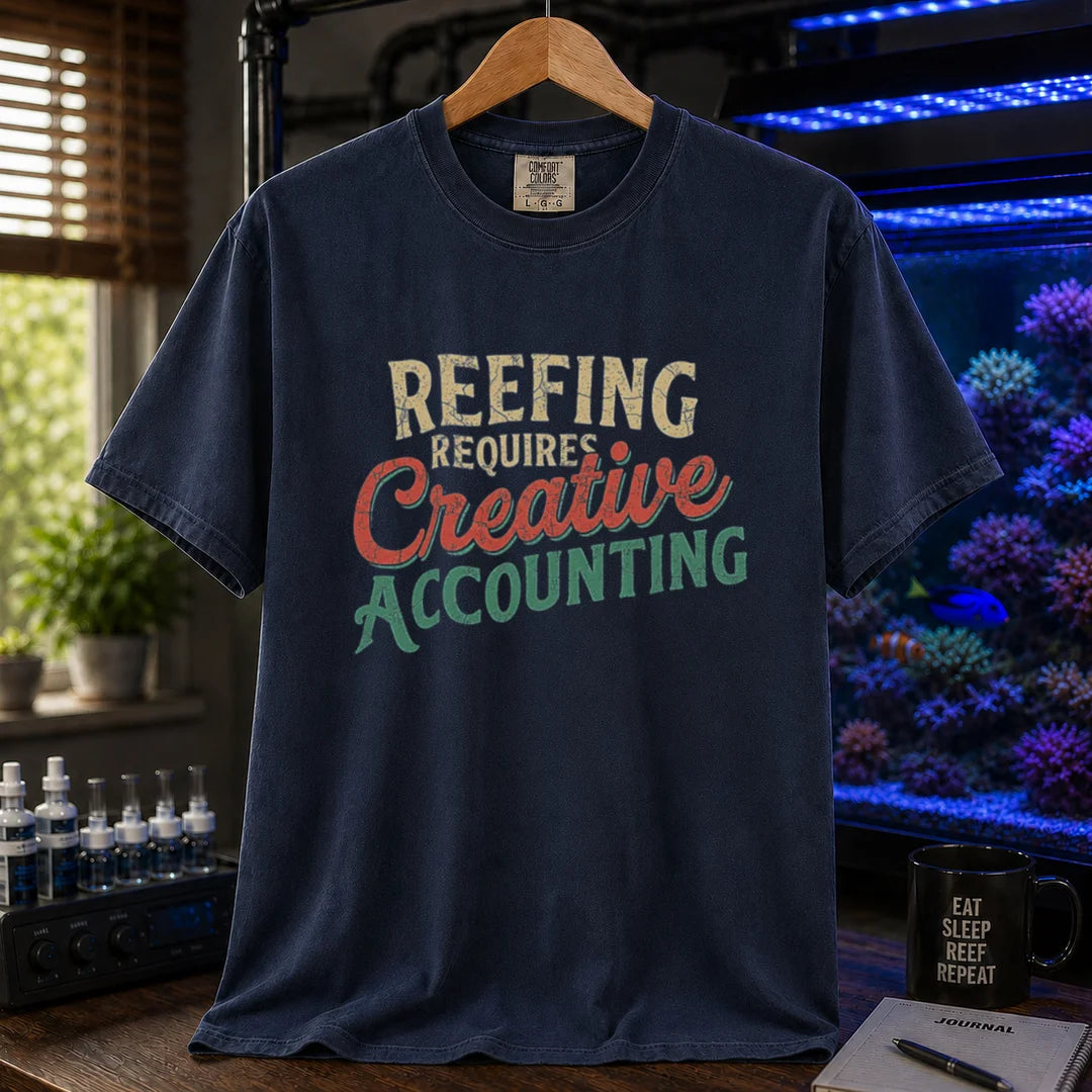 Saltwater aquarium graphic t-shirt featuring distressed retro typography in cream, red, and green reading Reefing Requires Creative Accounting, navy crew neck tee