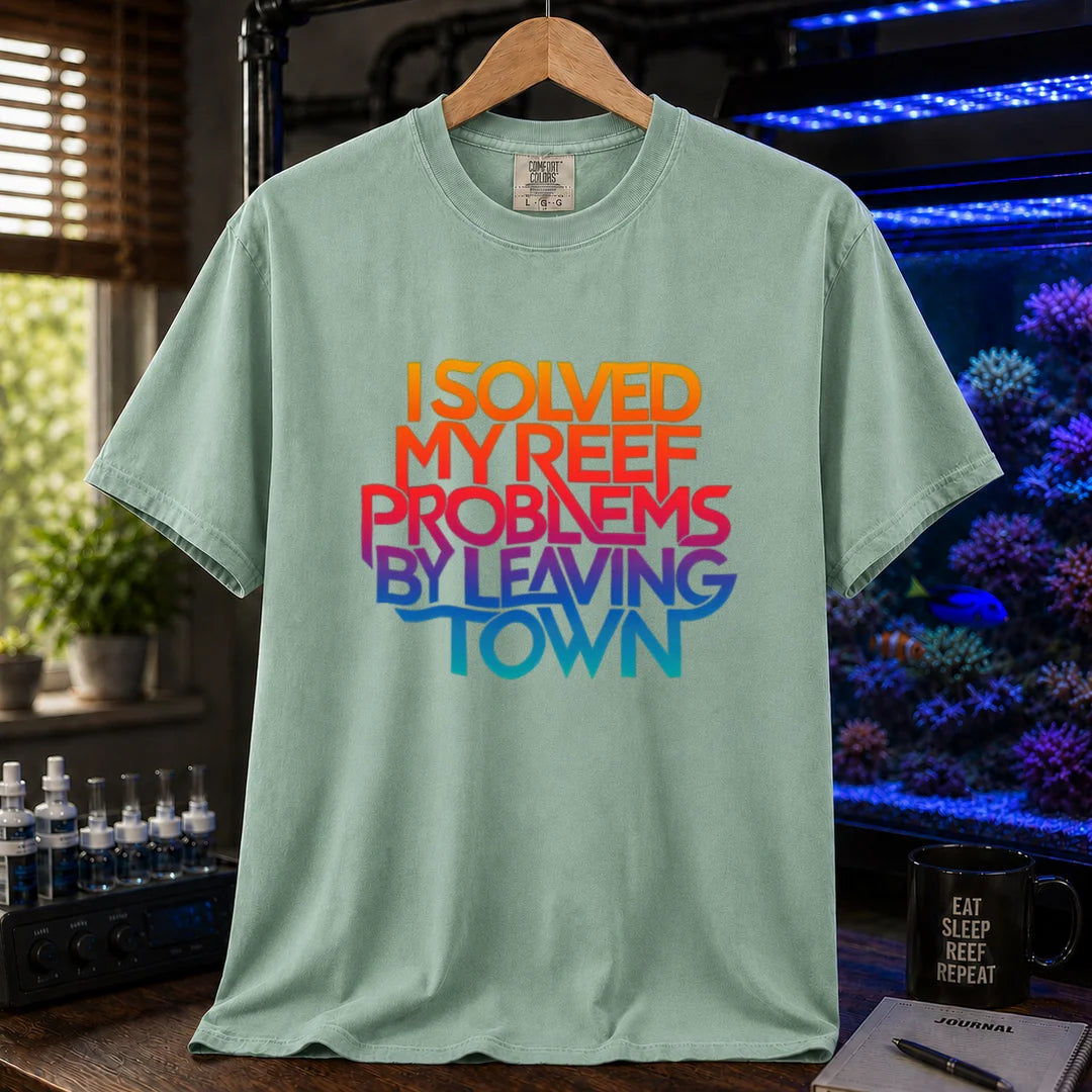 Saltwater aquarium graphic t-shirt featuring bold stacked gradient typography reading I Solved My Reef Problems By Leaving Town, green crew neck tee