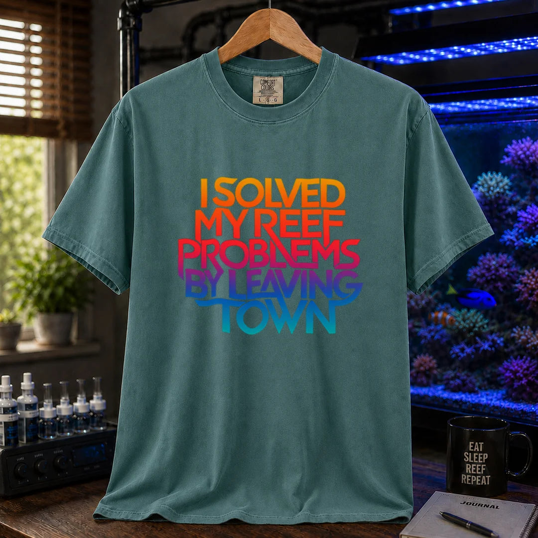 Saltwater aquarium graphic t-shirt featuring bold stacked gradient typography reading I Solved My Reef Problems By Leaving Town, green crew neck tee