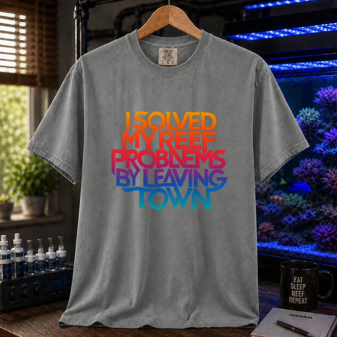 Saltwater aquarium graphic t-shirt featuring bold stacked gradient typography reading I Solved My Reef Problems By Leaving Town, grey crew neck tee