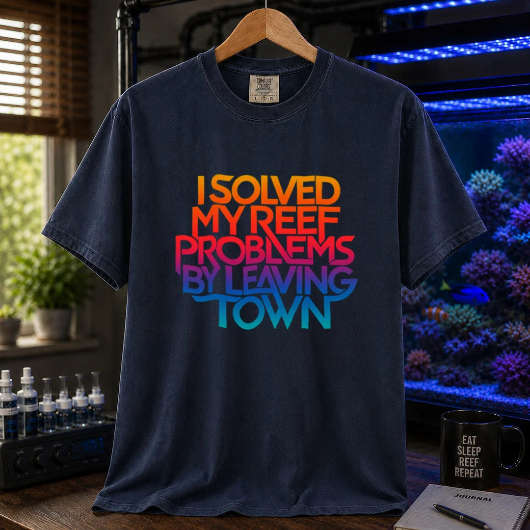 Saltwater aquarium graphic t-shirt featuring bold stacked gradient typography reading I Solved My Reef Problems By Leaving Town, navy crew neck tee