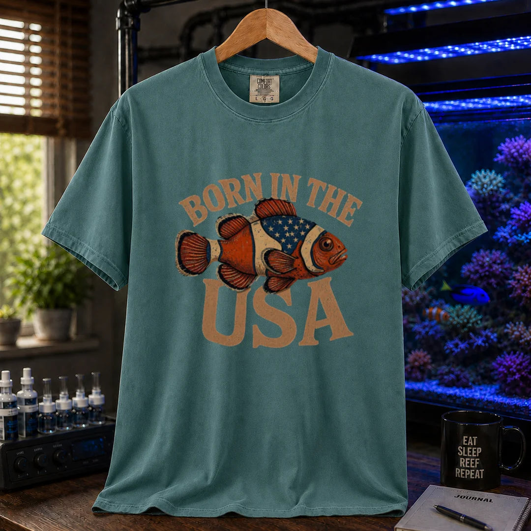 Saltwater aquarium graphic t-shirt featuring distressed vintage typography reading Born in the USA with an illustrated clownfish patterned like the American flag, green crew neck tee
