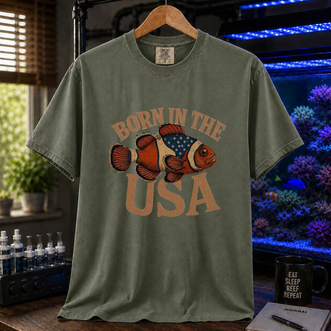 Saltwater aquarium graphic t-shirt featuring distressed vintage typography reading Born in the USA with an illustrated clownfish patterned like the American flag, military green crew neck tee