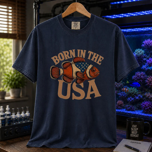 Saltwater aquarium graphic t-shirt featuring distressed vintage typography reading Born in the USA with an illustrated clownfish patterned like the American flag, navy crew neck tee