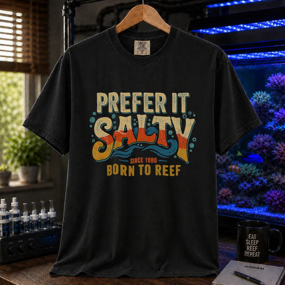 Saltwater aquarium graphic t-shirt featuring distressed retro typography in yellow, orange, and teal reading Prefer It Salty Born To Reef Since 1980 with wave graphics, black crew neck tee