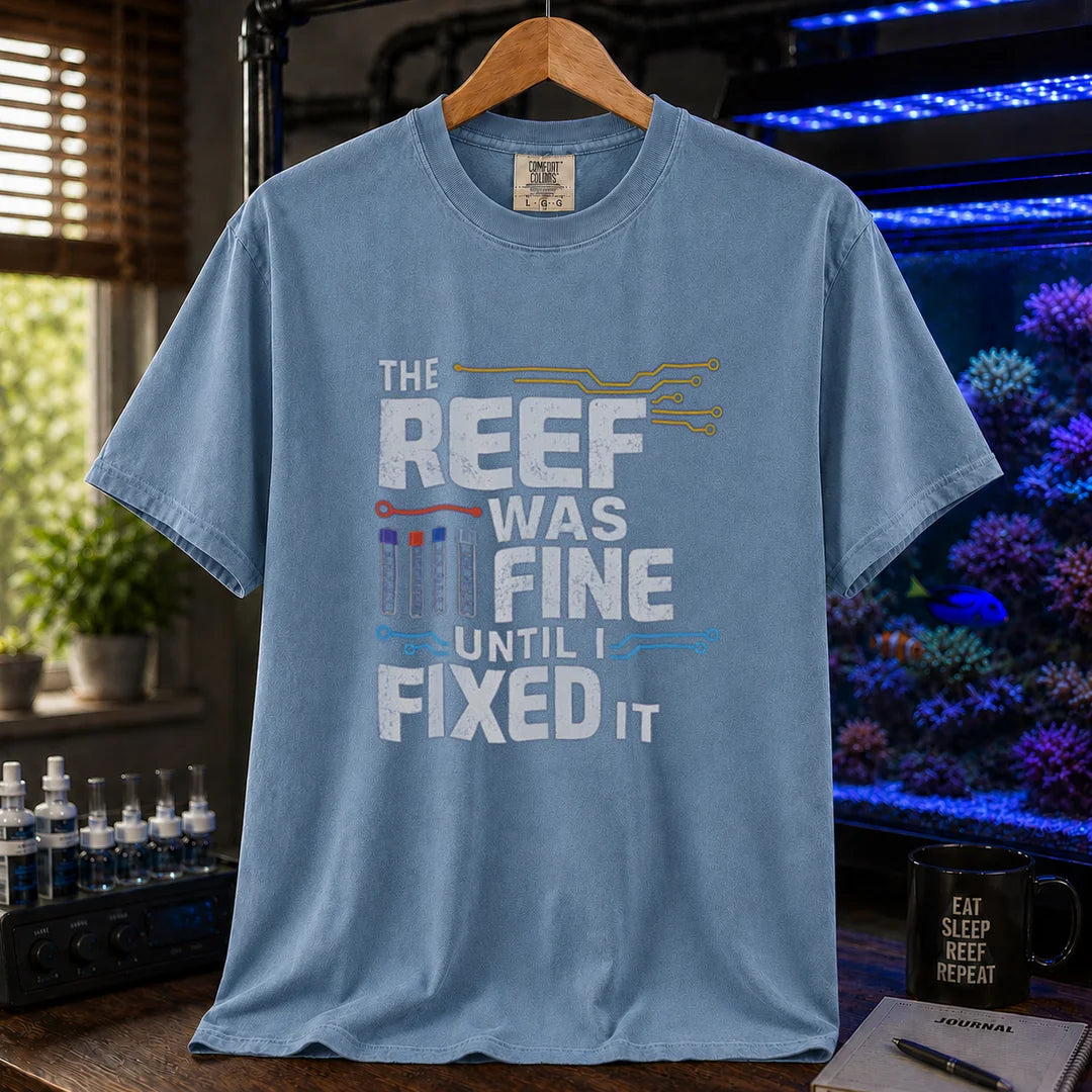 Saltwater aquarium graphic t-shirt featuring distressed white typography reading The Reef Was Fine Until I Fixed It with test vial icons and circuit lines, blue crew neck tee