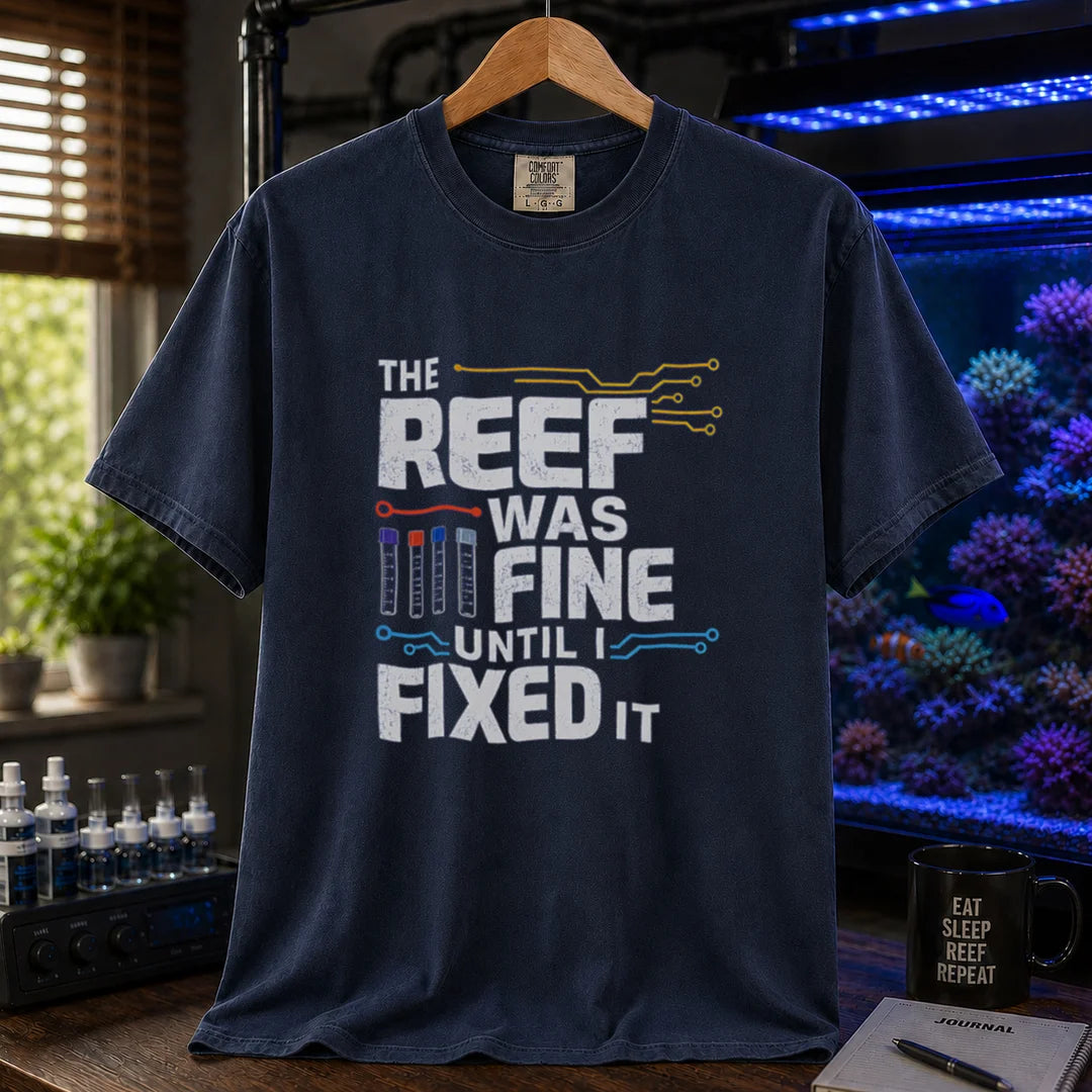 Saltwater aquarium graphic t-shirt featuring distressed white typography reading The Reef Was Fine Until I Fixed It with test vial icons and circuit lines, navy crew neck tee