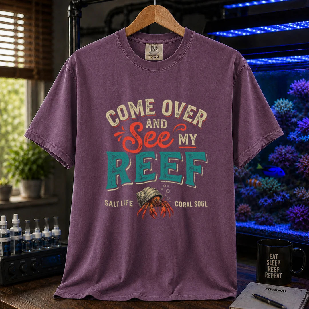 Saltwater aquarium graphic t-shirt featuring distressed retro typography reading Come Over And See My Reef with a hermit crab illustration and footer text, purple crew neck tee