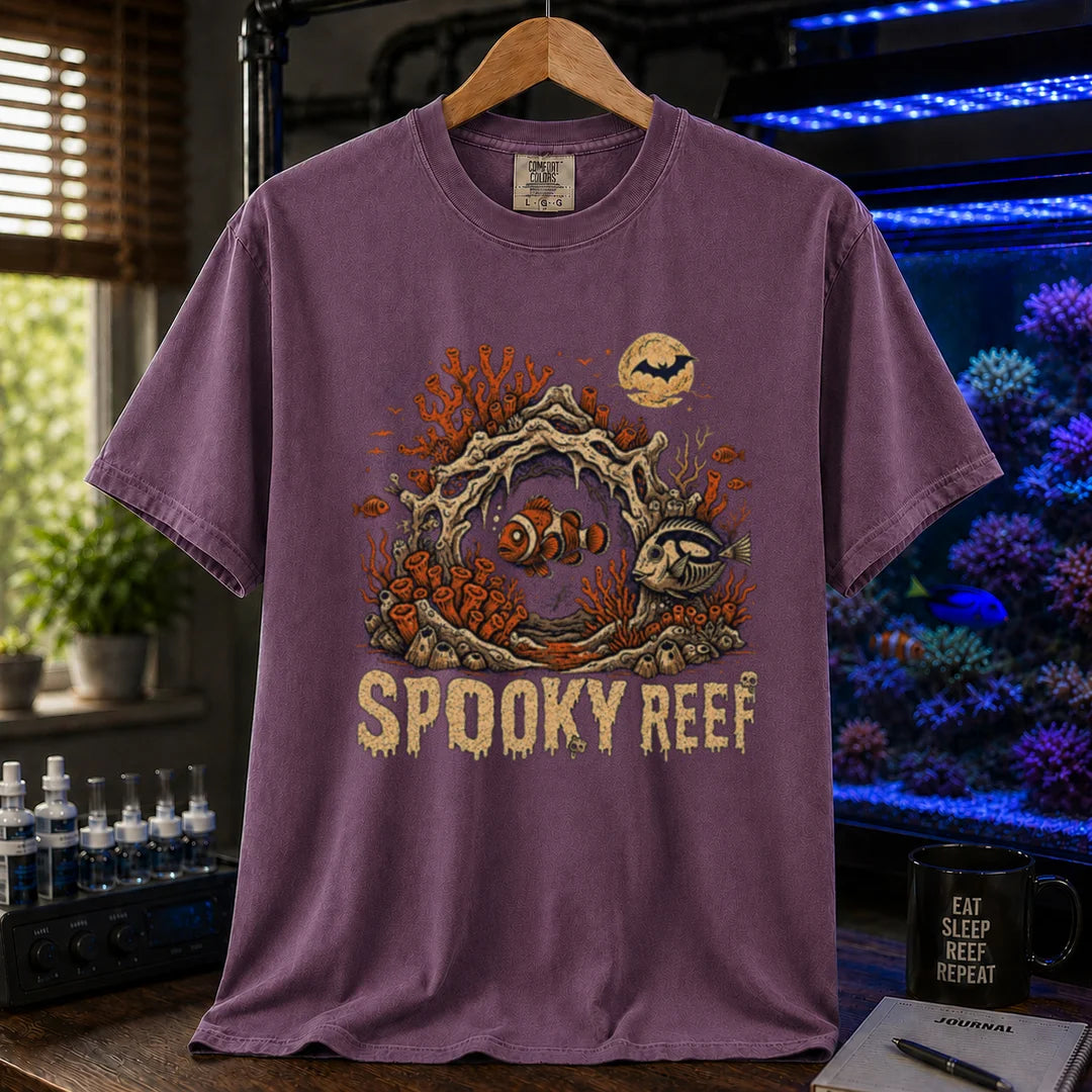 Saltwater aquarium graphic t-shirt design featuring dripping cream typography reading Spooky Reef with a spooky underwater scene featuring skeletal coral, a full moon with a bat, and eerie fish illustrations, purple crew neck tee