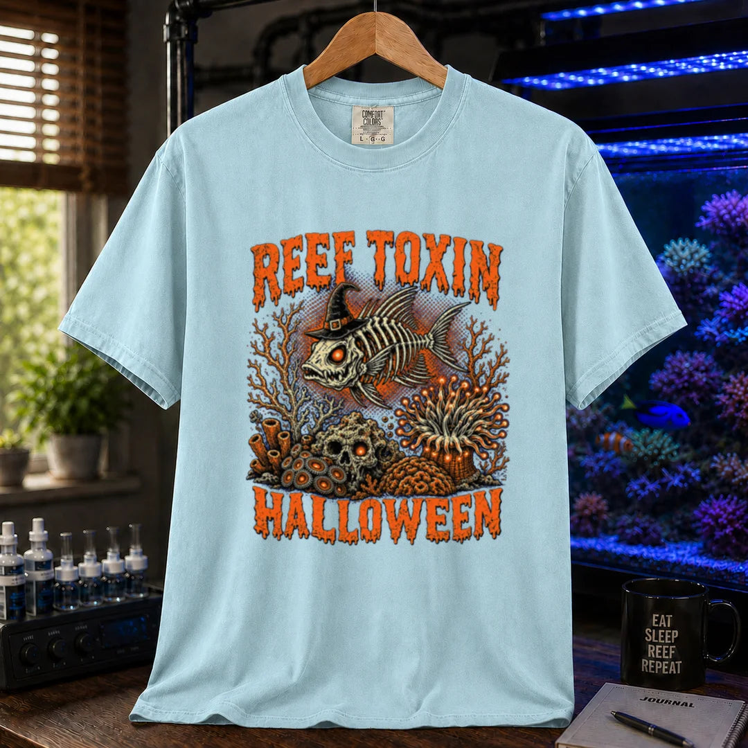 Saltwater aquarium graphic t-shirt design featuring dripping orange typography reading Reef Toxin Halloween with a witch-hat-wearing fish skeleton, glowing zoanthids, a skull in the rocks, and an anemone, light blue crew neck tee