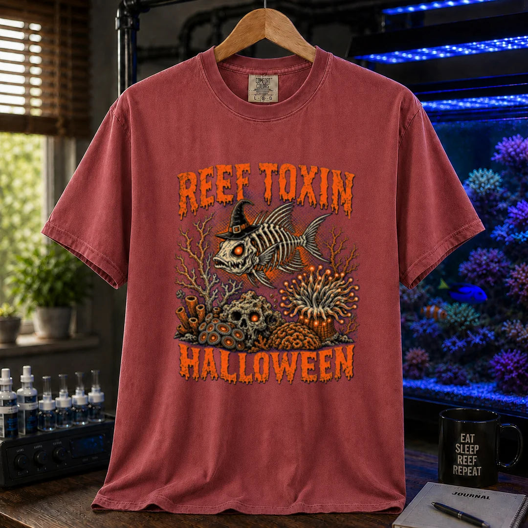 Saltwater aquarium graphic t-shirt design featuring dripping orange typography reading Reef Toxin Halloween with a witch-hat-wearing fish skeleton, glowing zoanthids, a skull in the rocks, and an anemone, maroon, red crew neck tee