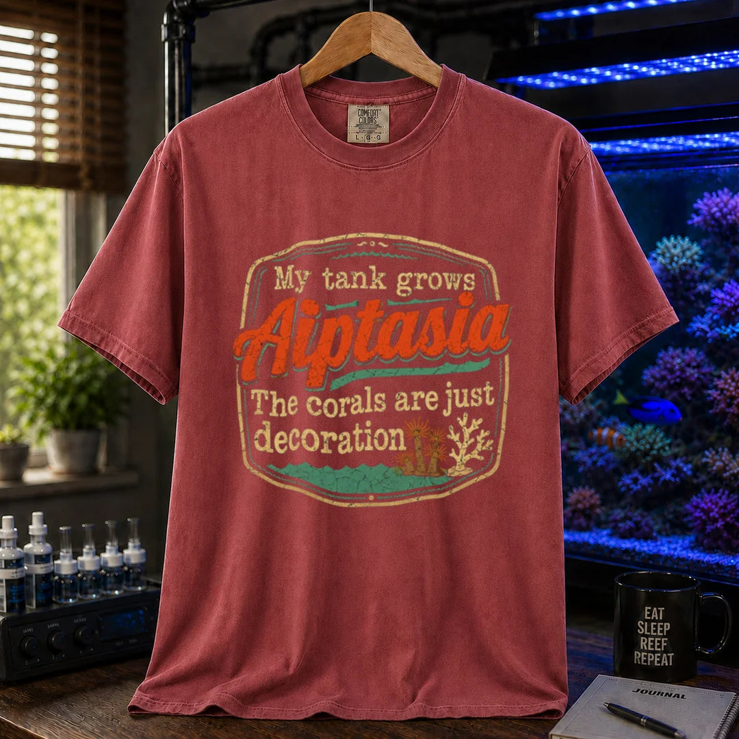 Saltwater aquarium graphic t-shirt design featuring a vintage badge reading My Tank Grows Aiptasia. The corals are just decoration with pest anemone illustrations on a maroon, red tee