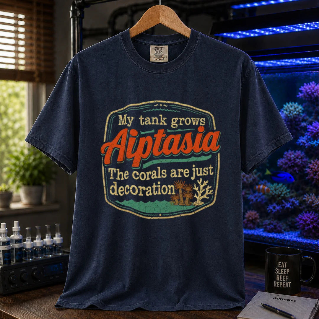 Saltwater aquarium graphic t-shirt design featuring a vintage badge reading My Tank Grows Aiptasia. The corals are just decoration with pest anemone illustrations on a NAVY tee