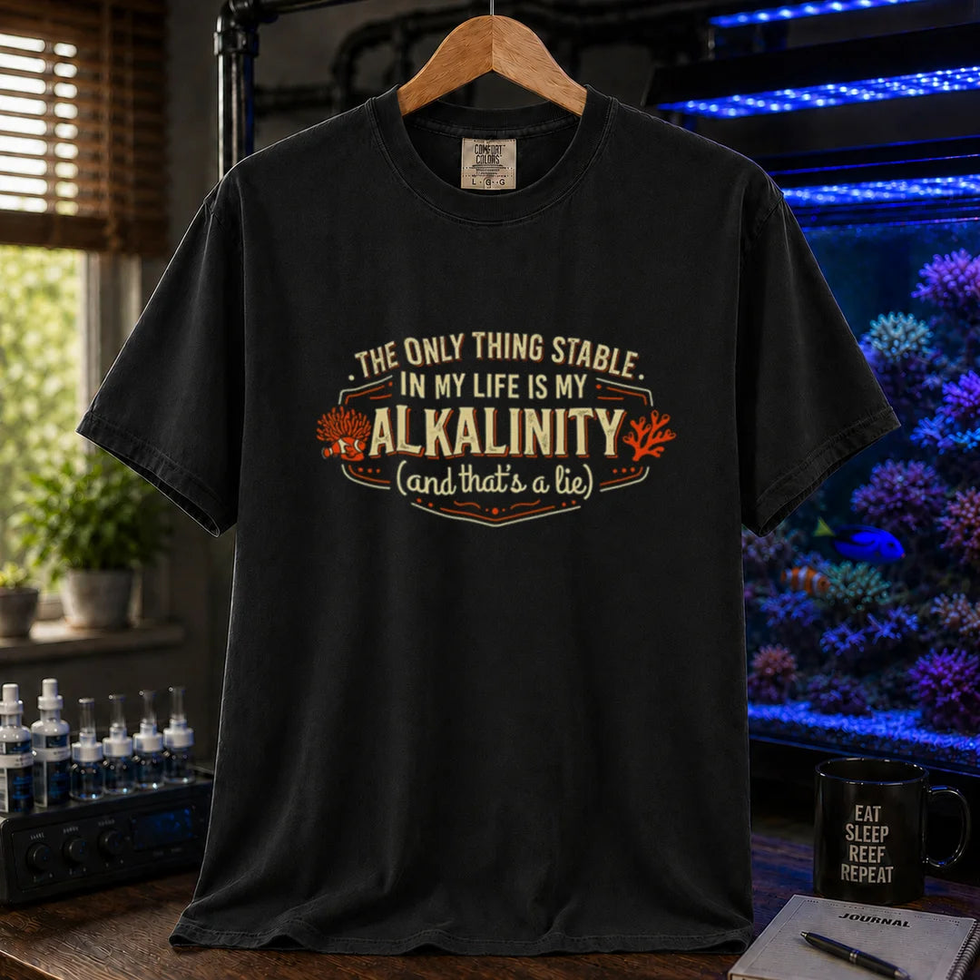 Saltwater aquarium graphic t-shirt design featuring a vintage badge reading The Only Thing Stable In My Life Is My Alkalinity (and that's a lie) with coral accents on a black tee