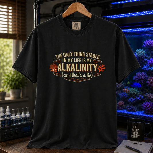 Saltwater aquarium graphic t-shirt design featuring a vintage badge reading The Only Thing Stable In My Life Is My Alkalinity (and that's a lie) with coral accents on a black tee