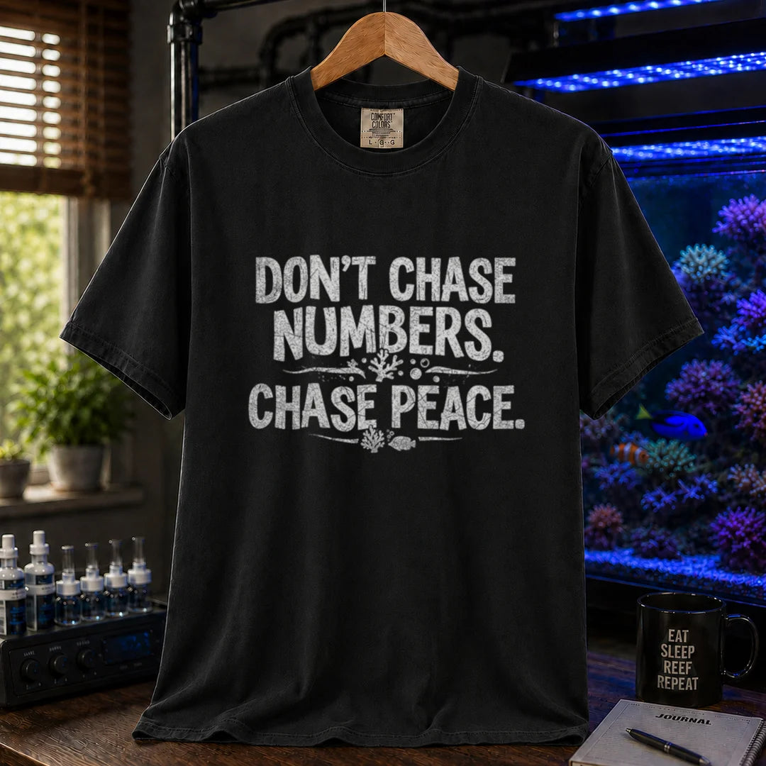 Saltwater aquarium graphic t-shirt design featuring distressed white typography reading Don't Chase Numbers. Chase Peace. with small coral and fish accents on a black tee