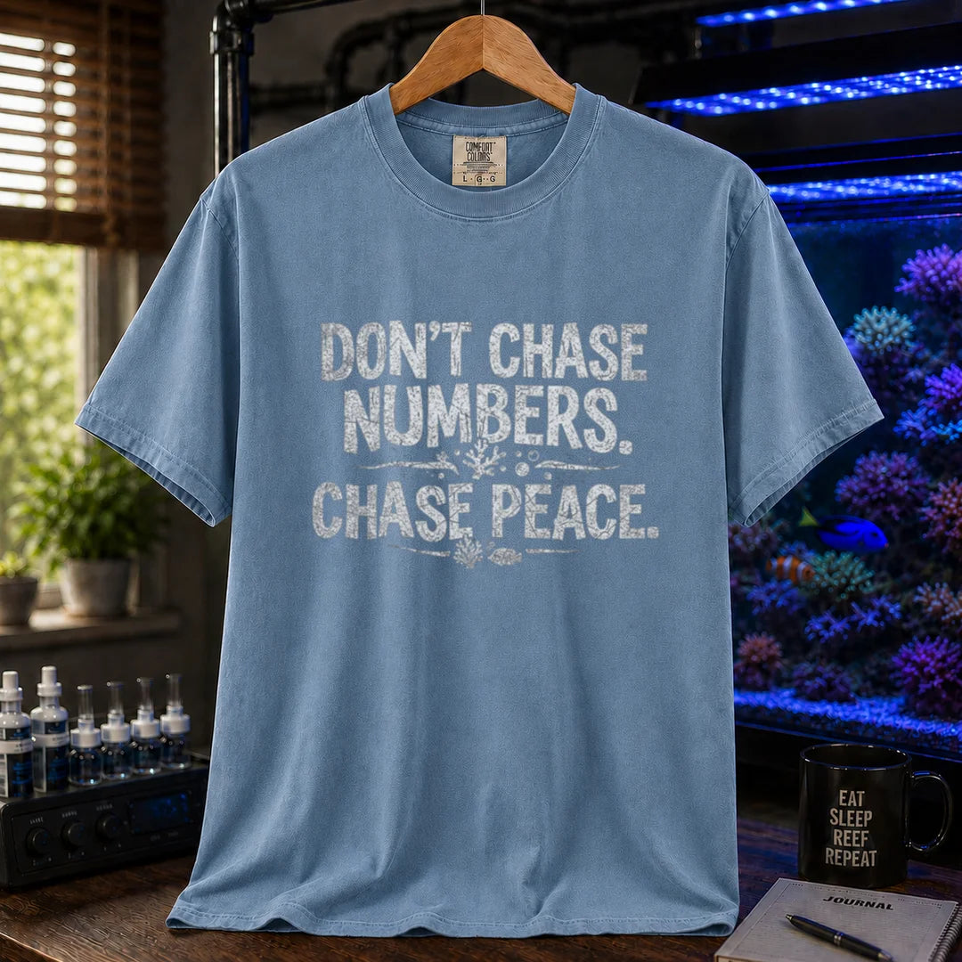Saltwater aquarium graphic t-shirt design featuring distressed white typography reading Don't Chase Numbers. Chase Peace. with small coral and fish accents on a blue tee