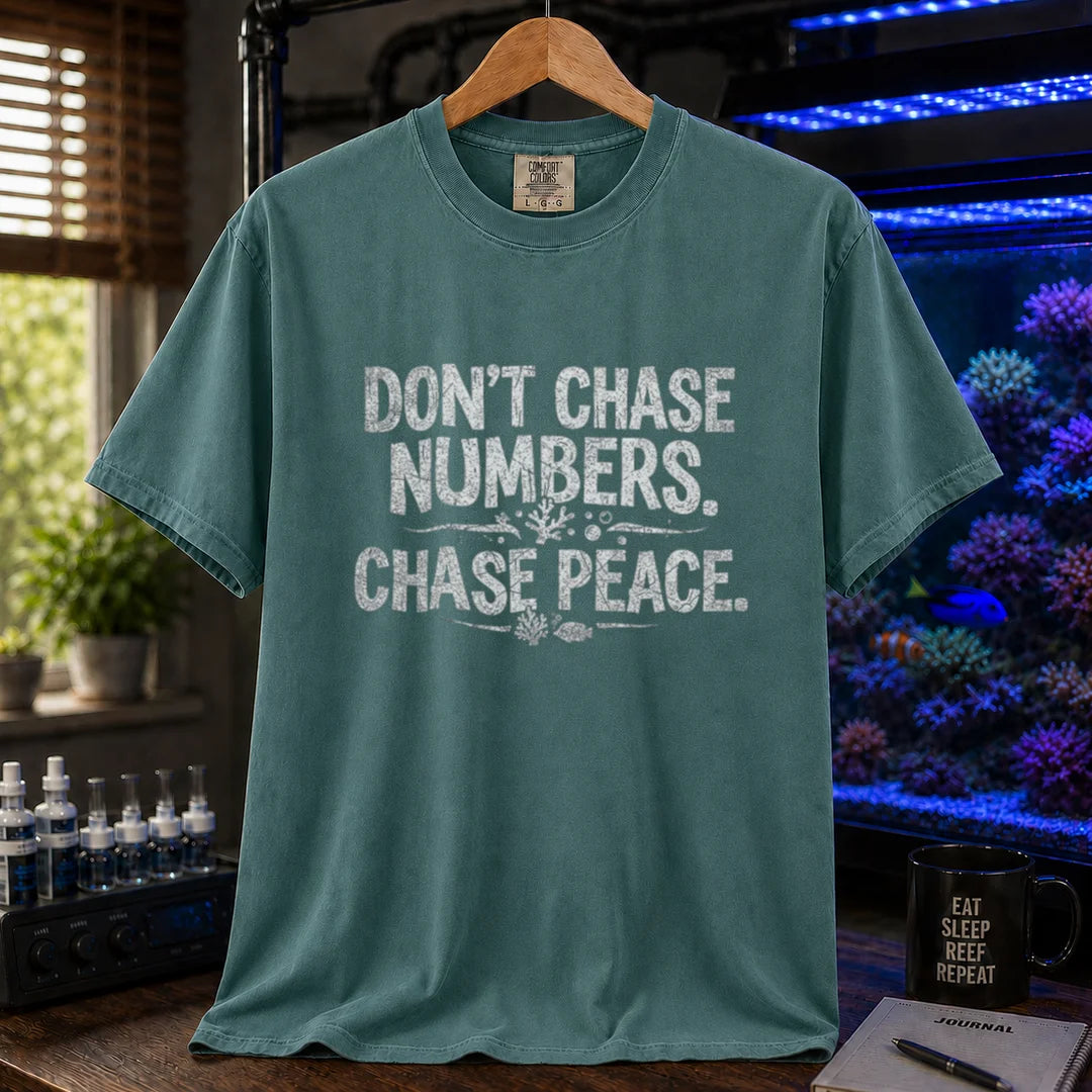 Saltwater aquarium graphic t-shirt design featuring distressed white typography reading Don't Chase Numbers. Chase Peace. with small coral and fish accents on a green tee
