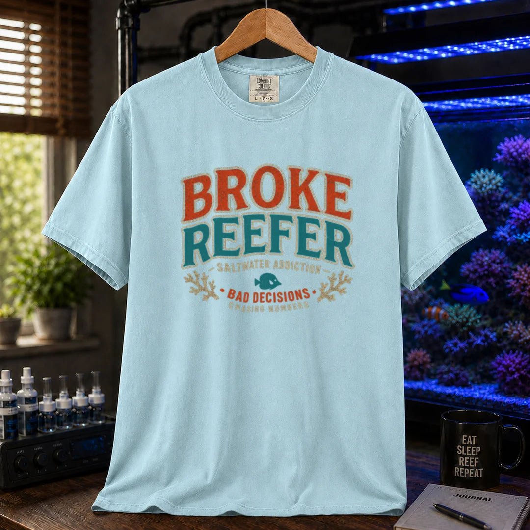 Saltwater aquarium graphic t-shirt design featuring a vintage badge reading Broke Reefer Saltwater Addiction Bad Decisions Chasing Numbers with coral and fish illustrations on a light blue tee