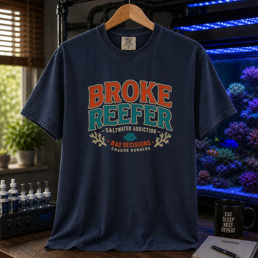 Saltwater aquarium graphic t-shirt design featuring a vintage badge reading Broke Reefer Saltwater Addiction Bad Decisions Chasing Numbers with coral and fish illustrations on a navy tee