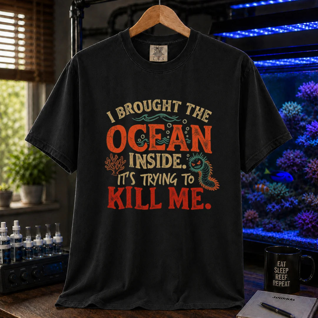 Saltwater aquarium graphic t-shirt design featuring distressed typography reading I Brought The Ocean Inside. It's Trying To Kill Me with a menacing bristle worm and coral illustration on a BLACK tee