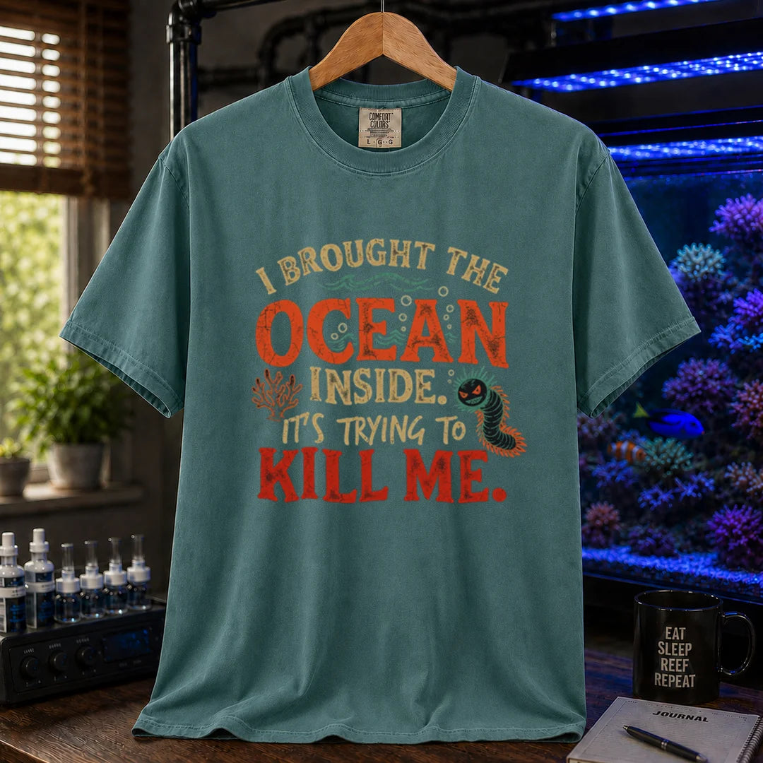Saltwater aquarium graphic t-shirt design featuring distressed typography reading I Brought The Ocean Inside. It's Trying To Kill Me with a menacing bristle worm and coral illustration on a green tee