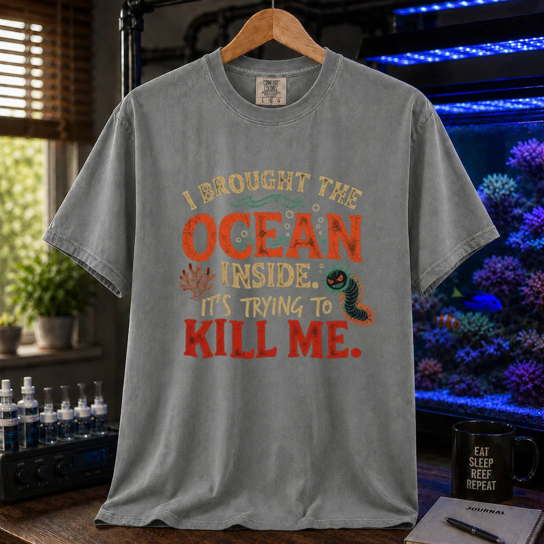 Saltwater aquarium graphic t-shirt design featuring distressed typography reading I Brought The Ocean Inside. It's Trying To Kill Me with a menacing bristle worm and coral illustration on a grey tee