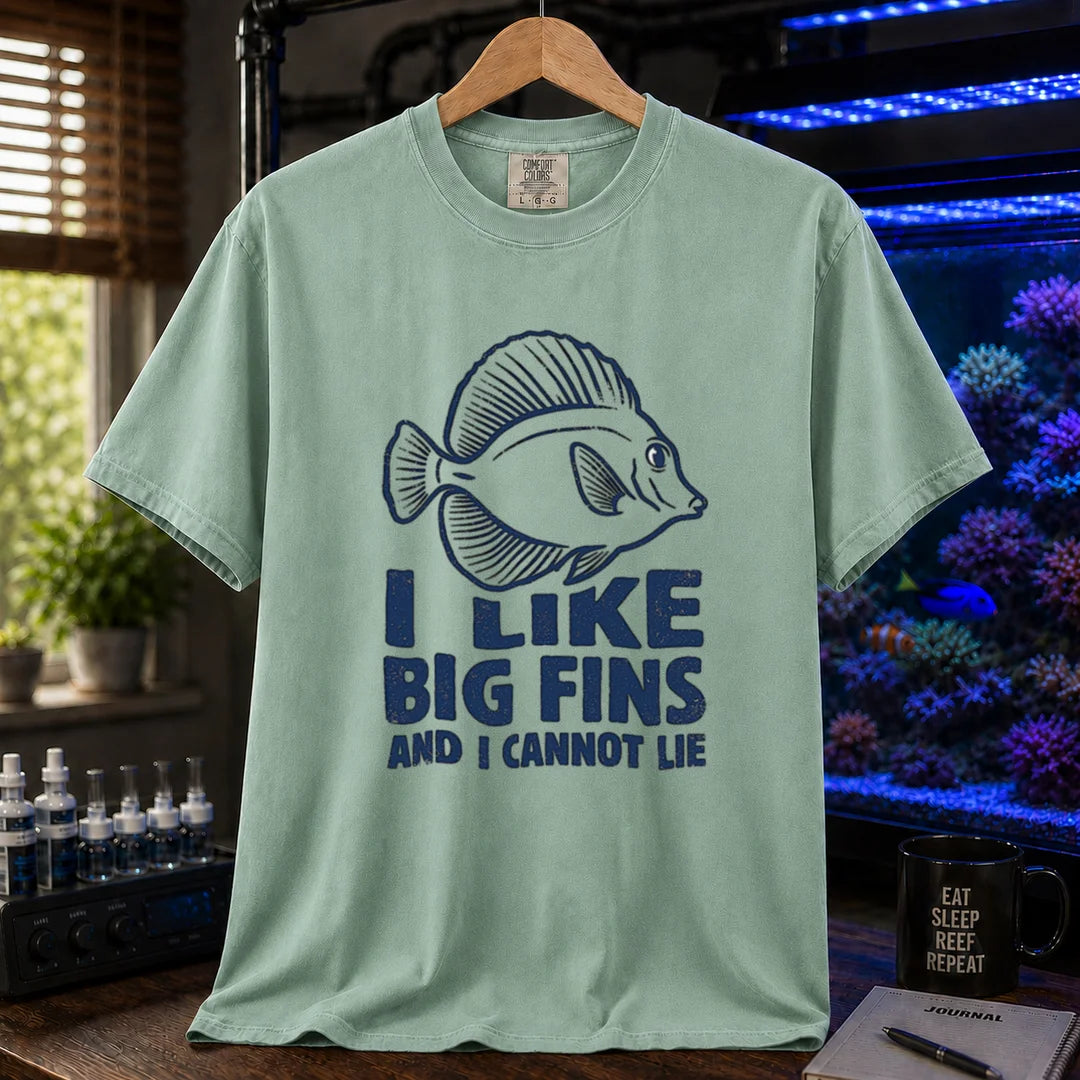 Saltwater aquarium graphic t-shirt design featuring distressed blue typography reading I Like Big Fins And I Cannot Lie with a detailed tang fish illustration on a light green tee