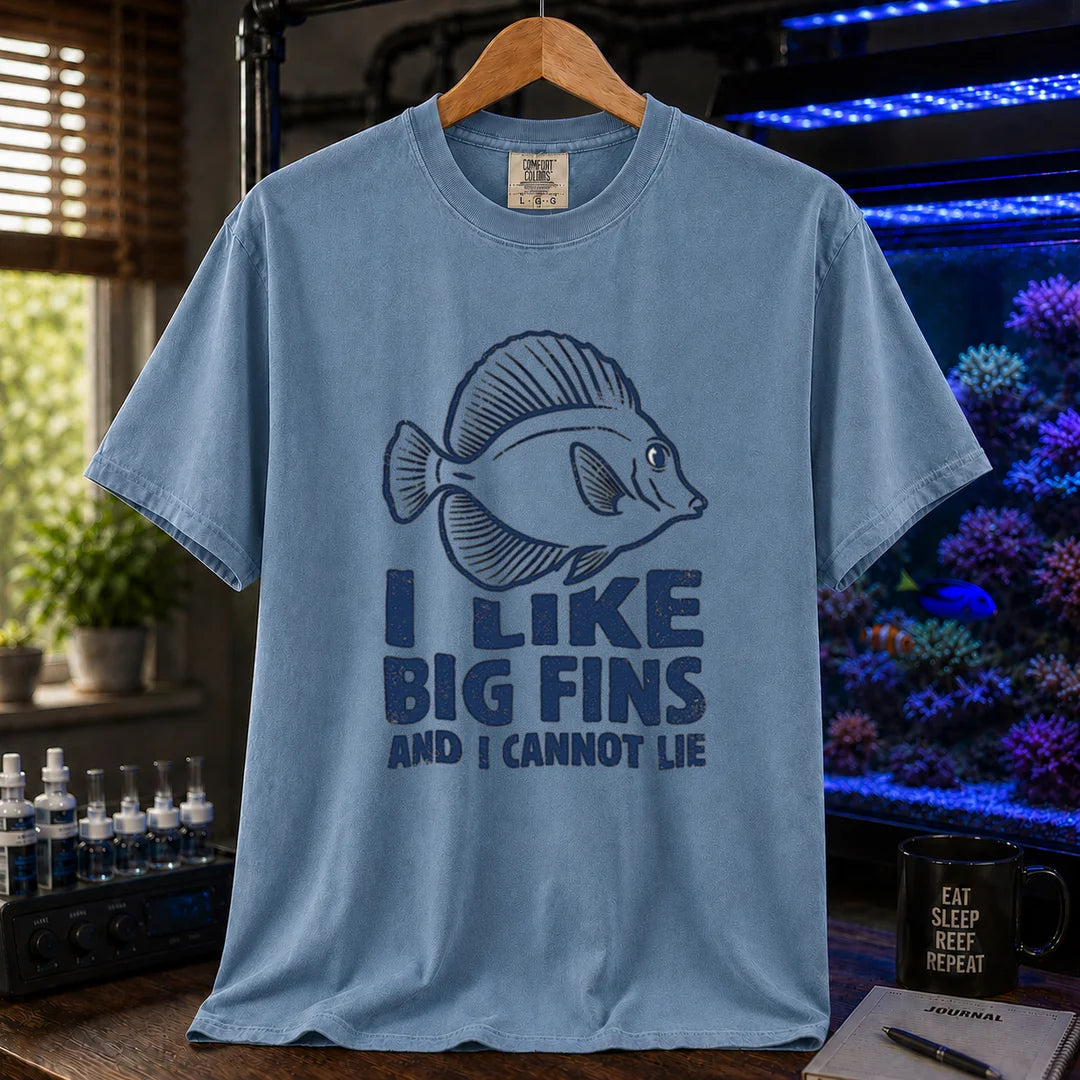 Saltwater aquarium graphic t-shirt design featuring distressed blue typography reading I Like Big Fins And I Cannot Lie with a detailed tang fish illustration on a blue tee