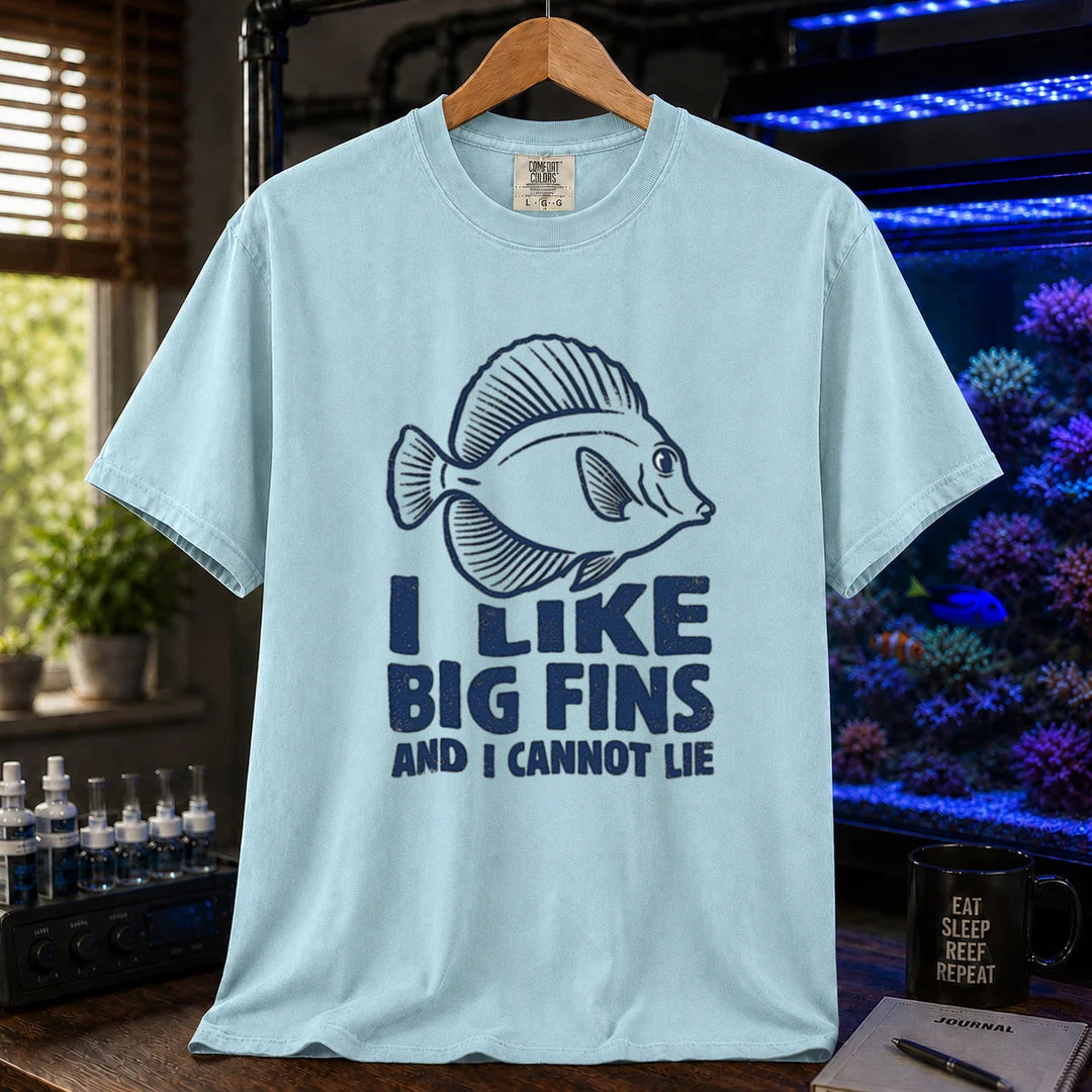 Saltwater aquarium graphic t-shirt design featuring distressed blue typography reading I Like Big Fins And I Cannot Lie with a detailed tang fish illustration on a light blue tee