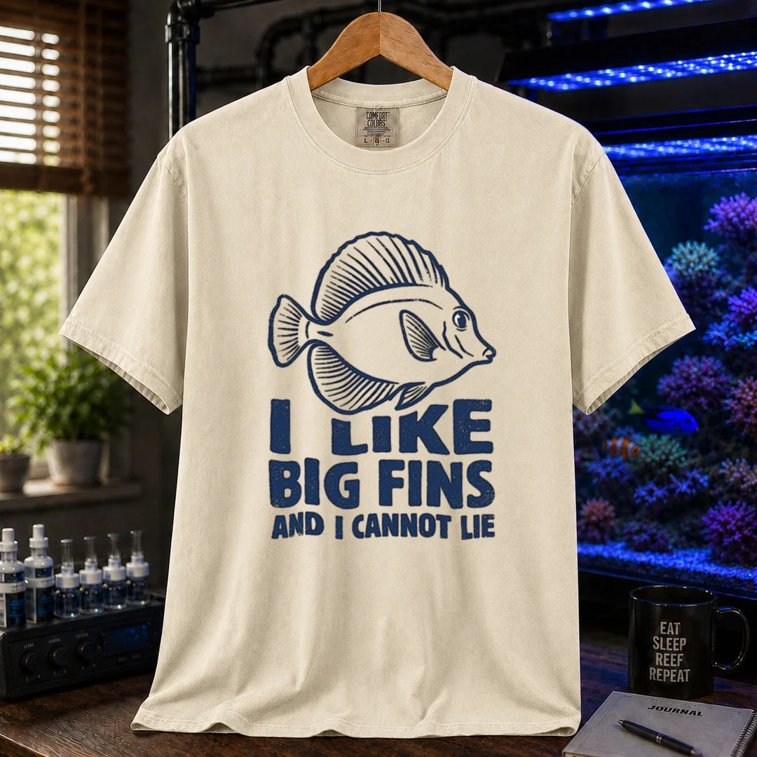 Saltwater aquarium graphic t-shirt design featuring distressed blue typography reading I Like Big Fins And I Cannot Lie with a detailed tang fish illustration on a beige, cream, ivory tee