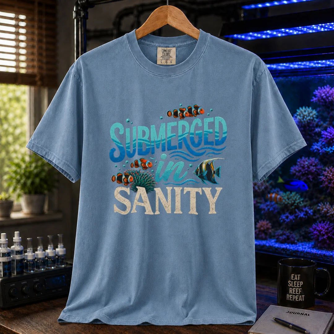 Saltwater aquarium graphic t-shirt design featuring wavy blue typography reading Submerged In Sanity with clownfish and coral artwork on a blue tee