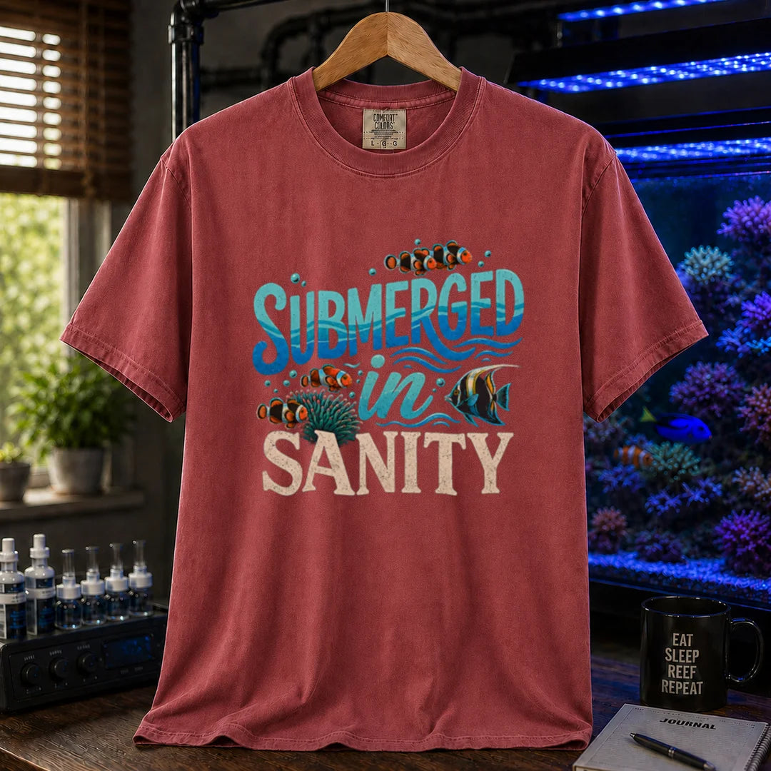 Saltwater aquarium graphic t-shirt design featuring wavy blue typography reading Submerged In Sanity with clownfish and coral artwork on a maroon, red tee
