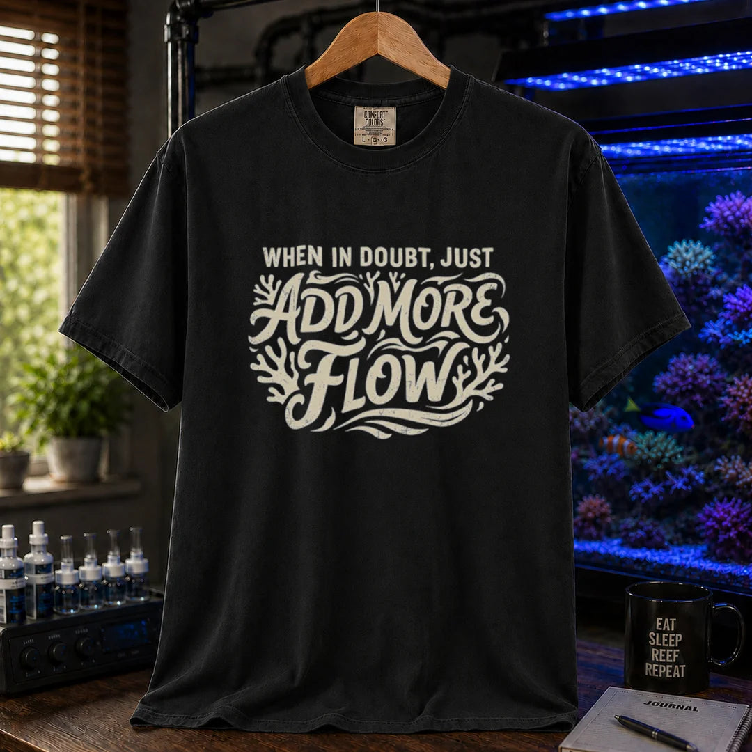 Saltwater aquarium graphic t-shirt featuring distressed cream typography reading When In Doubt, Just Add More Flow with coral accents printed on a black tee displayed in a reef room setting