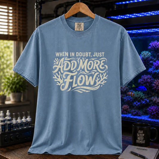 Saltwater aquarium graphic t-shirt featuring distressed cream typography reading When In Doubt, Just Add More Flow with coral accents printed on a blue tee displayed in a reef room setting