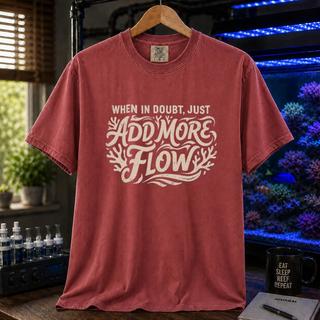 Saltwater aquarium graphic t-shirt featuring distressed cream typography reading When In Doubt, Just Add More Flow with coral accents printed on a maroon, red tee displayed in a reef room setting