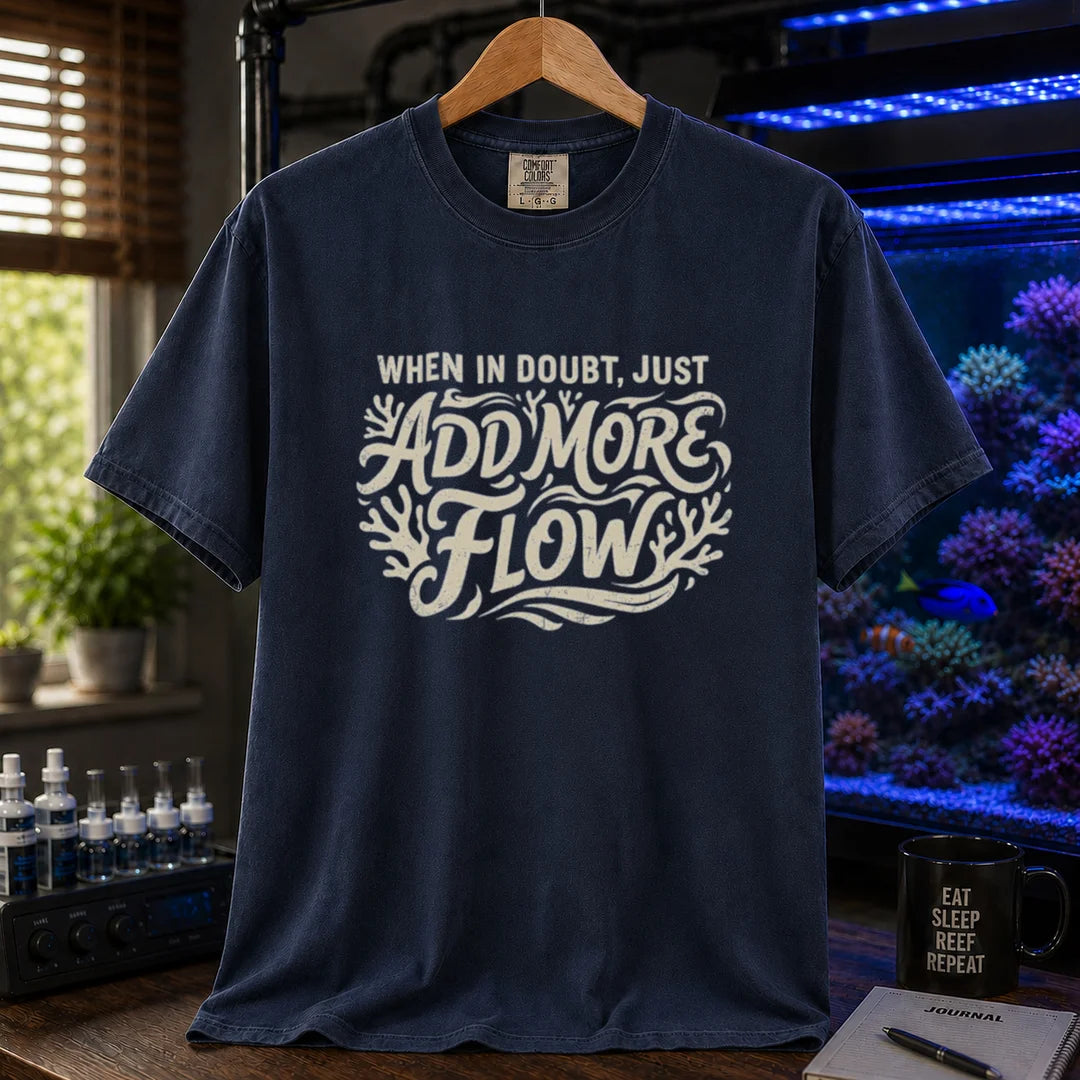 Saltwater aquarium graphic t-shirt featuring distressed cream typography reading When In Doubt, Just Add More Flow with coral accents printed on a navy tee displayed in a reef room setting