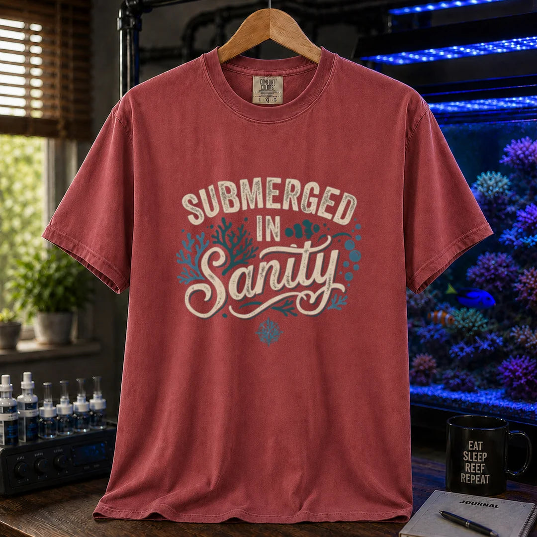Saltwater aquarium graphic t-shirt featuring distressed cream and teal typography reading Submerged In Sanity with coral and bubble accents printed on a maroon, red tee displayed in a reef room setting