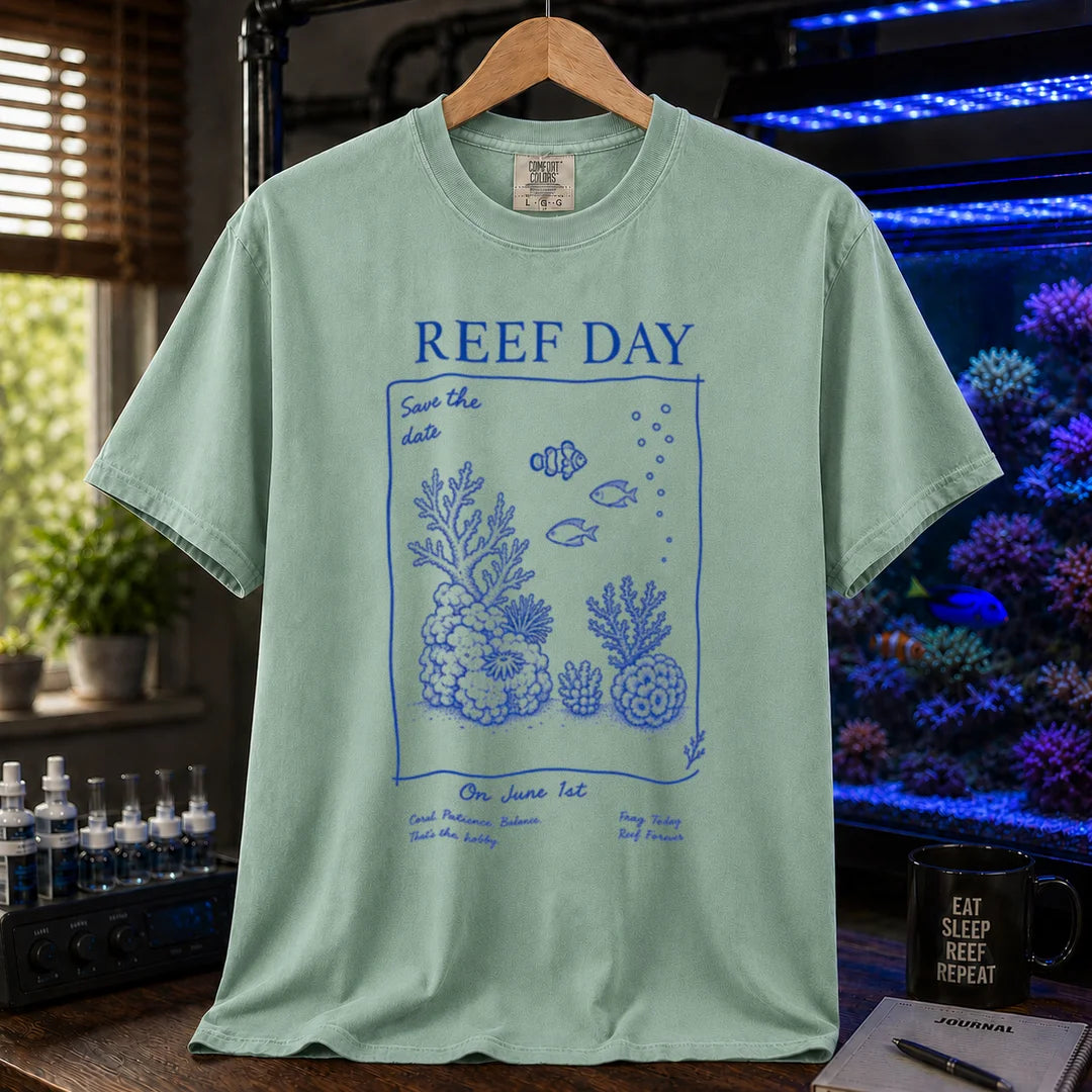 Saltwater aquarium graphic t-shirt featuring blue line-art typography and illustrations reading Reef Day Save The Date On June 1st with coral and fish graphics printed on a light green tee displayed in a reef room setting