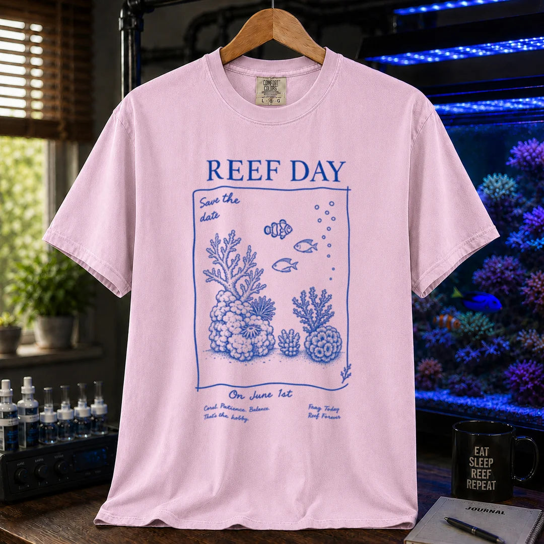 Saltwater aquarium graphic t-shirt featuring blue line-art typography and illustrations reading Reef Day Save The Date On June 1st with coral and fish graphics printed on a pink tee displayed in a reef room setting