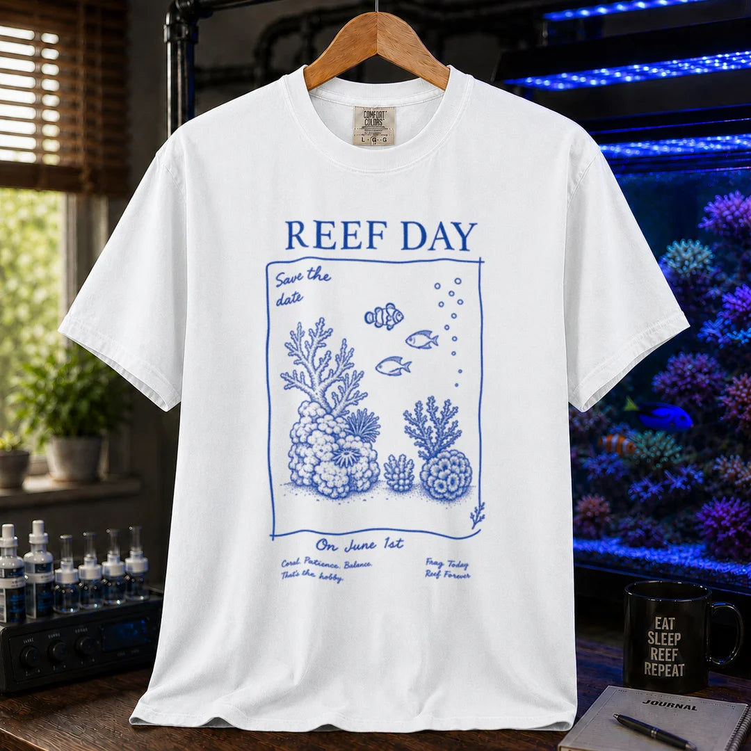 Saltwater aquarium graphic t-shirt featuring blue line-art typography and illustrations reading Reef Day Save The Date On June 1st with coral and fish graphics printed on a white tee displayed in a reef room setting