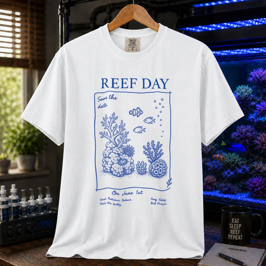 Saltwater aquarium graphic t-shirt featuring blue line-art typography and illustrations reading Reef Day Save The Date On June 1st with coral and fish graphics printed on a white tee displayed in a reef room setting