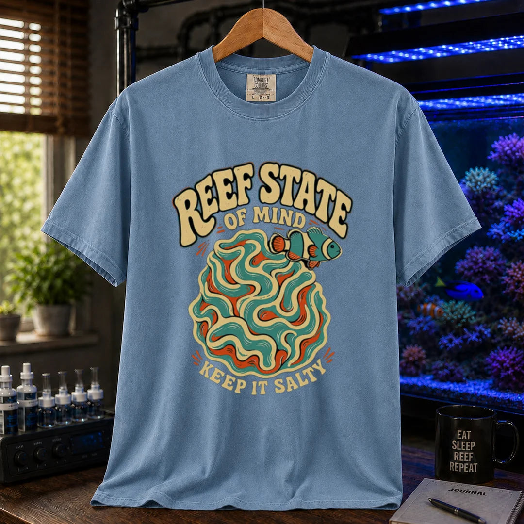 Saltwater aquarium graphic t-shirt featuring retro cream typography reading Reef State Of Mind Keep It Salty with a swirling abstract coral and clownfish design printed on a blue tee displayed in a reef room setting