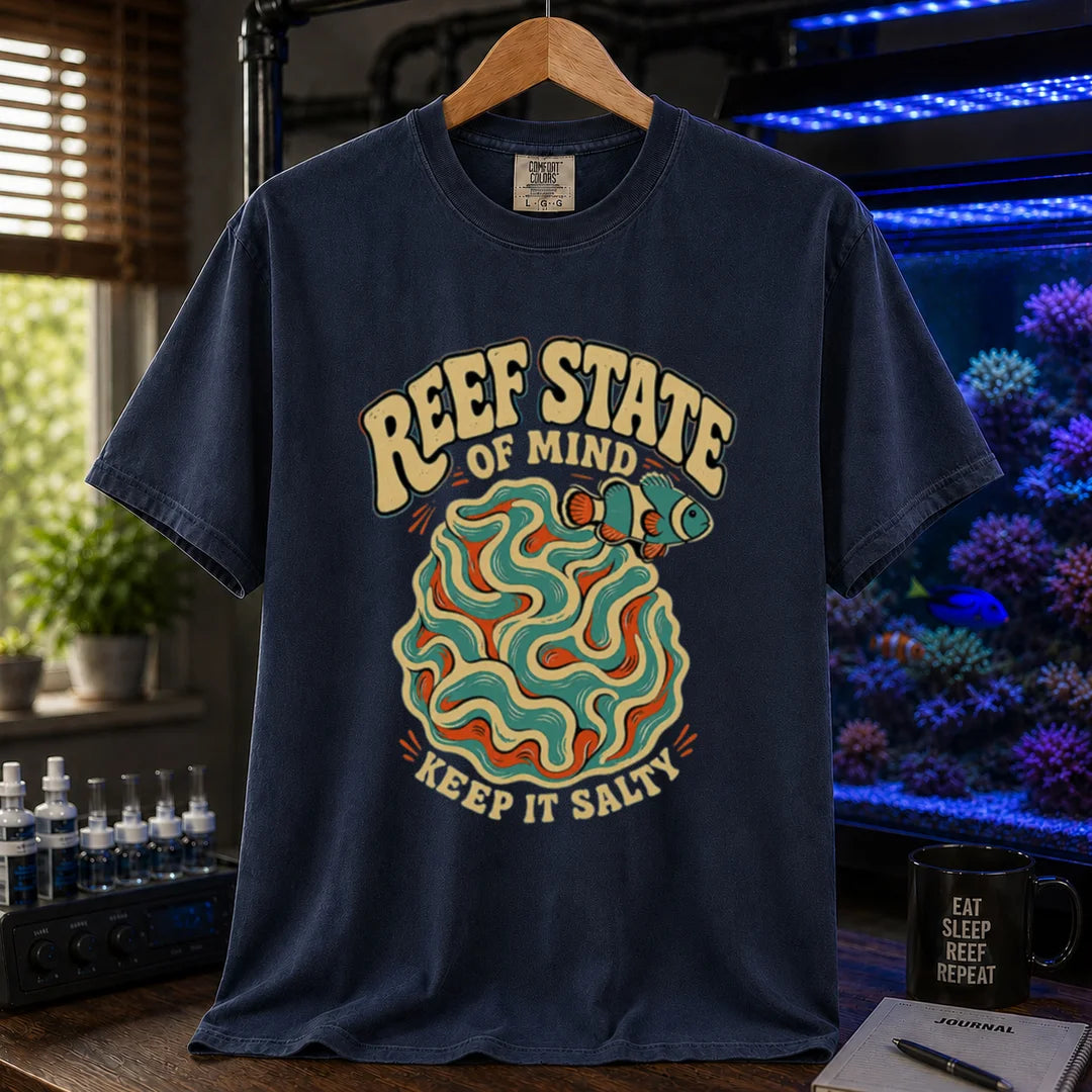 Saltwater aquarium graphic t-shirt featuring retro cream typography reading Reef State Of Mind Keep It Salty with a swirling abstract coral and clownfish design printed on a navy tee displayed in a reef room setting